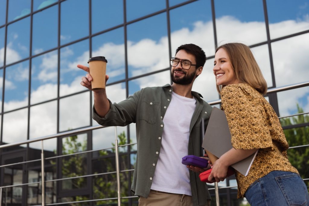 smiling young students with notebooks and coffee to go talking on campus